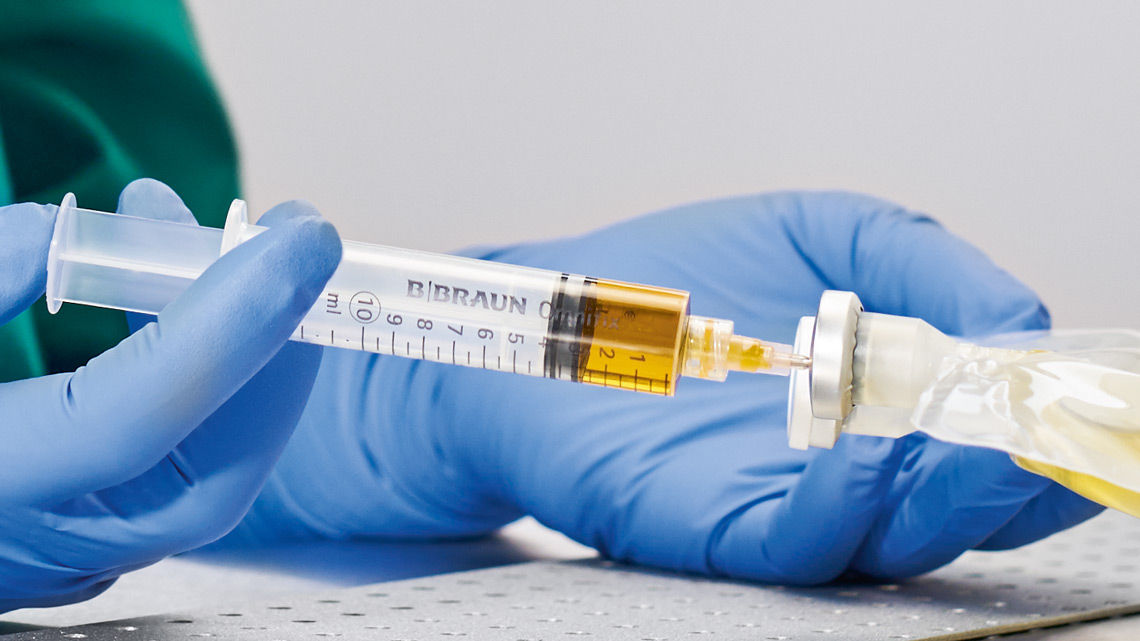 hands of a healthcare professional draws yellow liquid from a bottle using a syringe