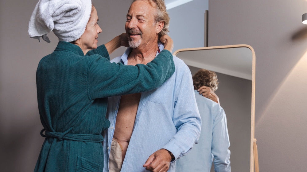 Wife in green bathrob hugs husband with the stoma bag