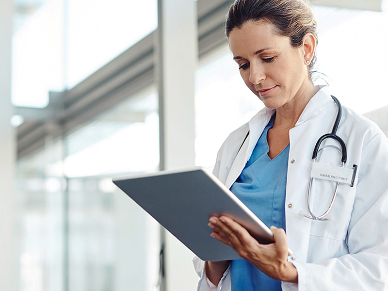 A female healthcare professional stands by a window, holding a tablet and reviewing information