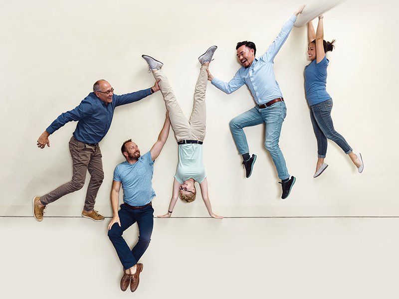  Five people striking different poses, with one person being held upside down by the others