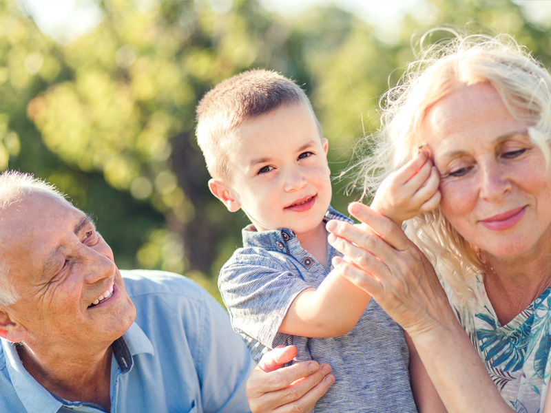 A middle-aged woman holding a small boy while a middle-aged man watches them and smiles