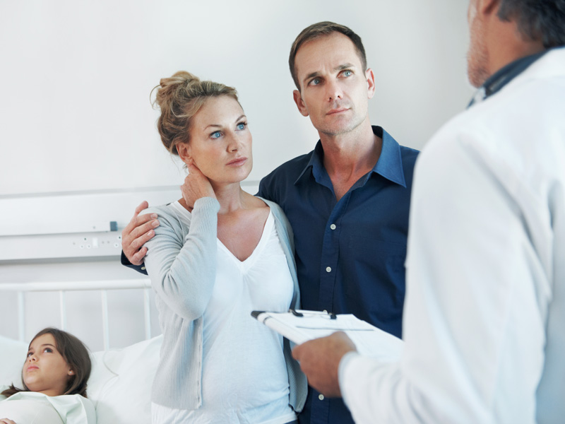  A male healthcare professional consulting with parents while their daughter lies in a hospital bed behind them