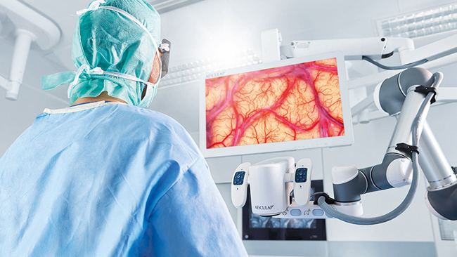 A surgeon performs a neurosurgery with the Aesculap Aeos® while standing tall and looking at the monitor. 