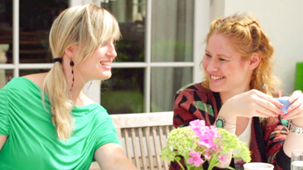 A woman smiles and talks with her friend in a garden while wearing a medical device to help with her hydrocephalus symptoms.