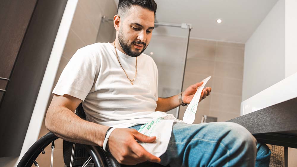 A patient sitting in a wheelchair holding a B. Braun catheter bag.