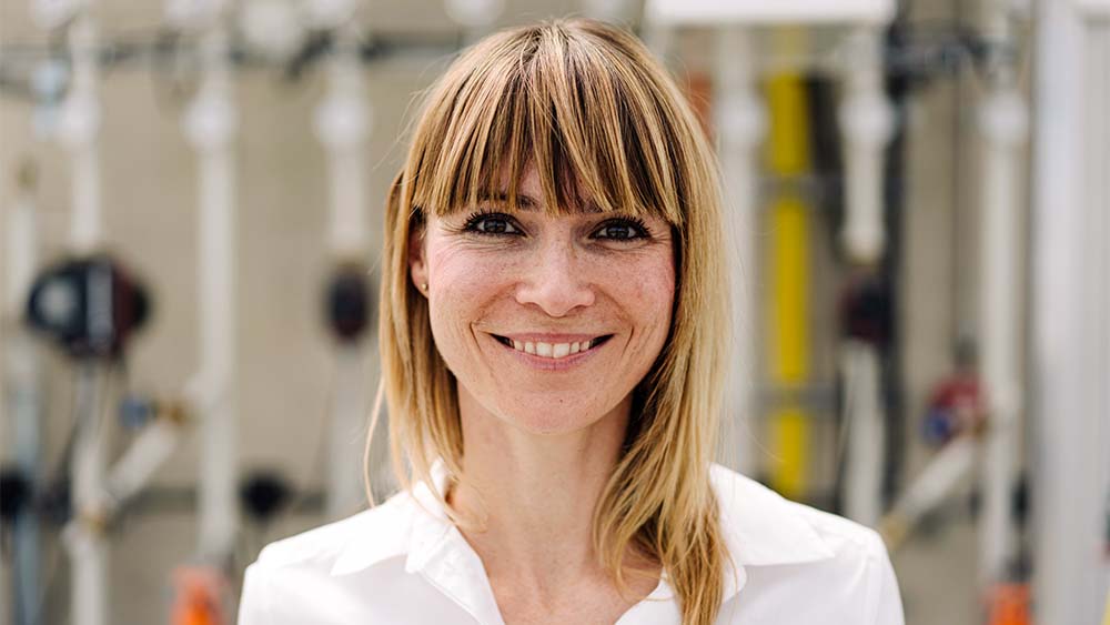 Close-up of a woman looking into the camera, smiling and wearing a white shirt in a bright setting. 